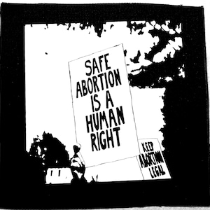 May include: Black and white image of a protest with a sign that reads "SAFE ABORTION IS A HUMAN RIGHT". A second sign reads "KEEP ABORTION LEGAL".