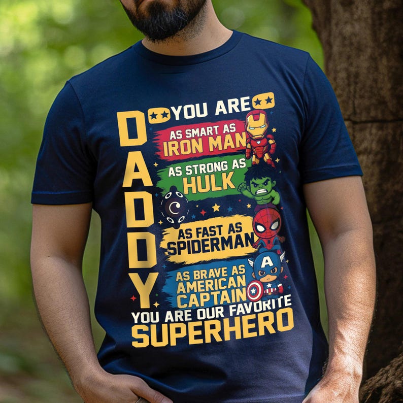 May include: Navy blue t-shirt with the word "DADDY" in yellow block letters. The shirt features colorful graphics of superheroes, including Iron Man, Hulk, Spiderman, and Captain America, with text that reads "You are our favorite superhero."
