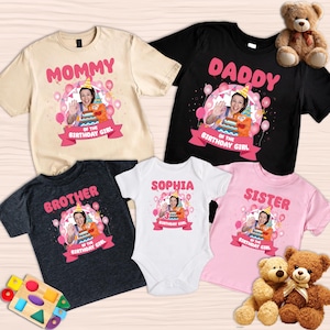 May include: A collection of personalized birthday shirts and a onesie. The shirts are beige, black, and charcoal gray, with the words "MOMMY", "DADDY", and "BROTHER" in pink. A white onesie says "SOPHIA". A pink shirt says "SISTER". Each shirt has a photo.