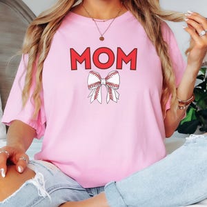 Peut inclure: T-shirt rose avec le mot "MOM" en lettres rouges et un n&oelig;ud rouge sur le th&egrave;me du baseball.