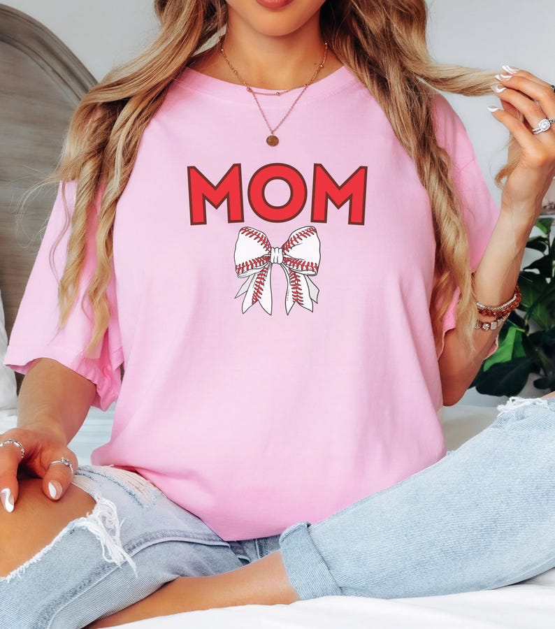 Peut inclure: T-shirt rose avec le mot "MOM" en lettres rouges et un n&oelig;ud rouge sur le th&egrave;me du baseball.