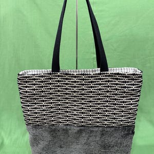 May include: A black and white patterned tote bag with a gray fabric bottom. The bag has black straps.