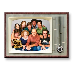 Puede incluir: Un televisor vintage con una pantalla que muestra el elenco del programa de televisión "That 70s Show". El elenco incluye un grupo de siete personas, incluyendo un hombre con bigote y una mujer con cabello largo y castaño.