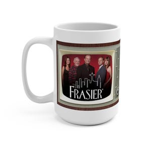 Może przedstawiać: Biały ceramiczny kubek z motywem ekranu telewizora, na którym widnieje logo i aktorzy serialu "Frasier". Kubek ma duży uchwyt i nadaje się do gorących napojów.