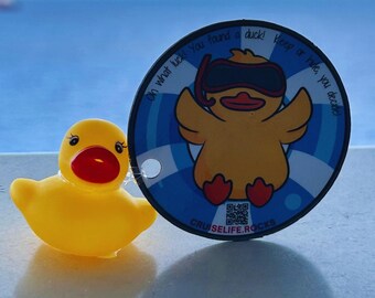May include: A yellow rubber duck with a red beak and a blue and white circular tag. The tag features a cartoon duck wearing a snorkel and the text "Oh what luck! You found a duck! Keep or hide, you decide!"