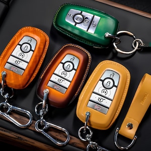 May include: Several car key fobs in shades of orange, brown, yellow, and green. Each key has a silver key ring and a leather strap. The keys feature silver buttons and a keyless entry system.