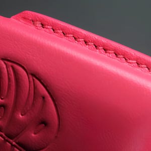 May include: Close-up of a bright pink leather phone case. The case features a stitched edge and an embossed design. The leather appears smooth and the stitching is a contrasting color. The case is a vibrant accessory.