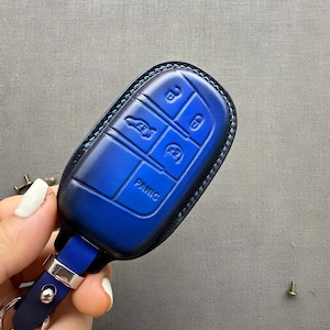 May include: A blue leather car key fob cover with embossed buttons and the word "PANIC". The fob has a silver metal loop and a blue leather strap. The key fob is designed to protect the car key.