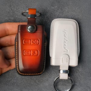 May include: Two key fobs, one brown leather and one white with the word "Vanquish" printed on it. The brown fob has buttons and a key ring. The white fob also has a key ring.