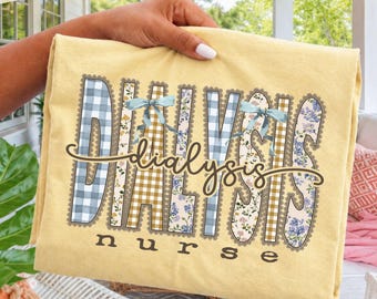 Puede incluir: Una camiseta de color amarillo pálido con la palabra DIALYSIS en letras grandes y decorativas con patrones variados que incluyen cuadros vichy azules, cuadros amarillos y estampados florales. La palabra nurse aparece debajo con lazos azules.