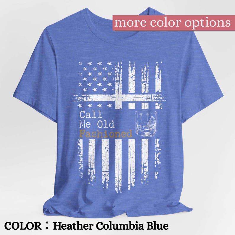 May include: A heather Columbia blue short-sleeve t-shirt featuring a white distressed American flag graphic. The design includes the text "Call Me Old Fashioned" in white and gold, accompanied by a line drawing of a glass with a citrus wedge.