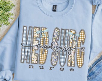 Puede incluir: Una sudadera de cuello redondo en color azul claro con el texto MED SURG en letras grandes estampadas con borde festoneado. Las letras incluyen cuadros vichy azules, flores y cuadros beige. La palabra nurse aparece debajo en marrón oscuro.