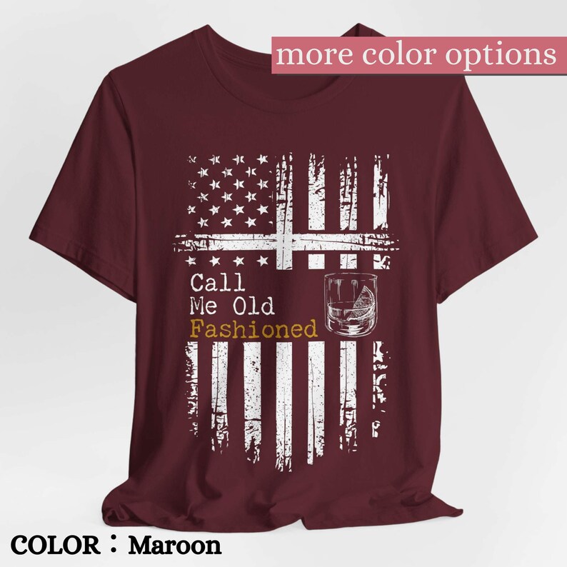 May include: A maroon short-sleeved t-shirt featuring a white distressed graphic of the American flag. The design includes a line drawing of a glass with a citrus wedge and the text Call Me Old Fashioned in white and gold lettering.