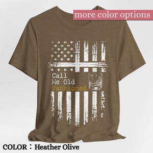 May include: A heather olive t-shirt featuring a distressed white graphic of the American flag. The design includes the text Call Me Old Fashioned in white and gold lettering, alongside a line drawing of a cocktail glass with a citrus wedge.