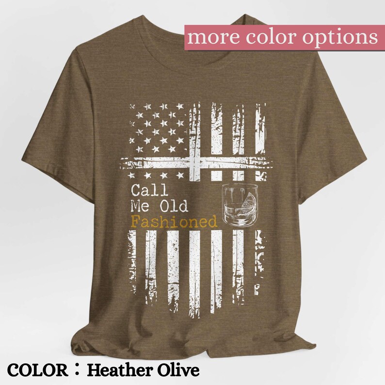 May include: A heather olive t-shirt featuring a distressed white graphic of the American flag. The design includes the text Call Me Old Fashioned in white and gold lettering, alongside a line drawing of a cocktail glass with a citrus wedge.