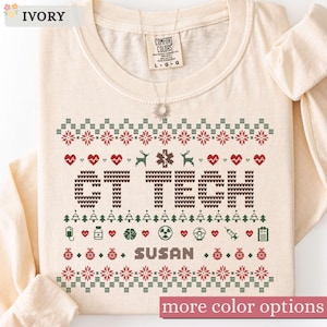 May include: An ivory long-sleeve shirt featuring a festive holiday-themed graphic with the text CT TECH and SUSAN. The design includes red and green patterns of hearts, medical symbols, trees, and ornaments in a knit-style print on the front.