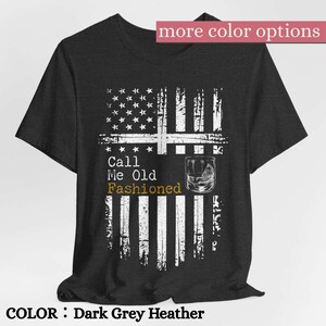 May include: A dark grey heather short-sleeve t-shirt featuring a distressed white graphic of an American flag. The text reads Call Me Old Fashioned, with the word Fashioned in gold, accompanied by a line drawing of a glass with a citrus wedge.