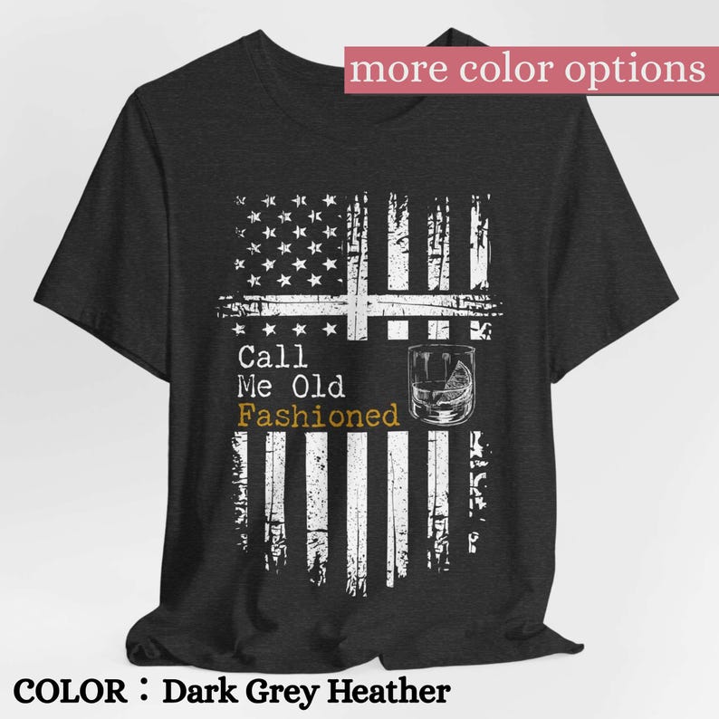 May include: A dark grey heather short-sleeve t-shirt featuring a distressed white graphic of an American flag. The text reads Call Me Old Fashioned, with the word Fashioned in gold, accompanied by a line drawing of a glass with a citrus wedge.