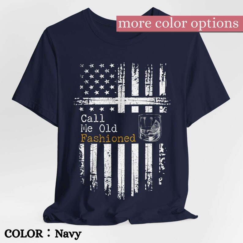 May include: A navy blue short-sleeve t-shirt featuring a distressed white graphic of the American flag. The design includes a cocktail glass illustration and the text Call Me Old Fashioned in white and gold lettering on the front center.