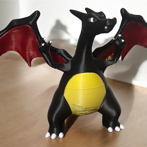 Könnte beinhalten: Eine schwarze 3D-gedruckte Figur eines Drachen mit roten Flügeln und einem gelben Bauch. Der Drache steht auf einer Holzoberfläche.