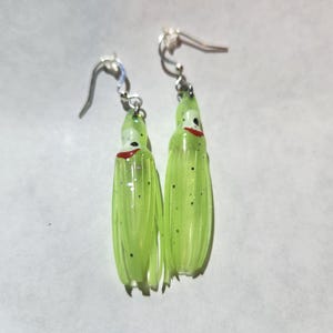 May include: A pair of green and white squid lure earrings with silver hooks. The lures have black glitter and red accents.
