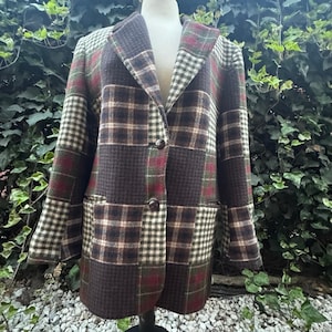 May include: A patchwork blazer in shades of brown, green, and red, featuring various plaid and houndstooth patterns. The blazer has a classic notched collar, two front pockets, and two buttons for closure. The garment is displayed on a mannequin.