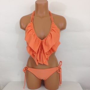 May include: A two-piece orange bikini set. The top features a halter neck and a ruffled design across the chest. The bottom is a classic bikini cut with tie sides. The set is displayed on a mannequin against a white background.