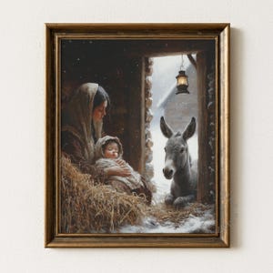 May include: A framed print depicting a serene nativity scene. A woman cradles a baby wrapped in a blanket, seated on hay. A donkey rests nearby in a snowy doorway, illuminated by a hanging lantern. The artwork is framed in a gold-toned wooden frame.