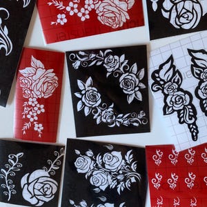 May include: A selection of vinyl decals with floral patterns. The decals showcase white rose and leaf designs on red and black backgrounds. Various shapes and sizes are present, some with a grid backing.