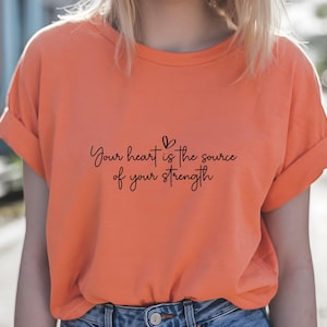 May include: A bright orange t-shirt with the text "Your heart is the source of your strength" printed in black.