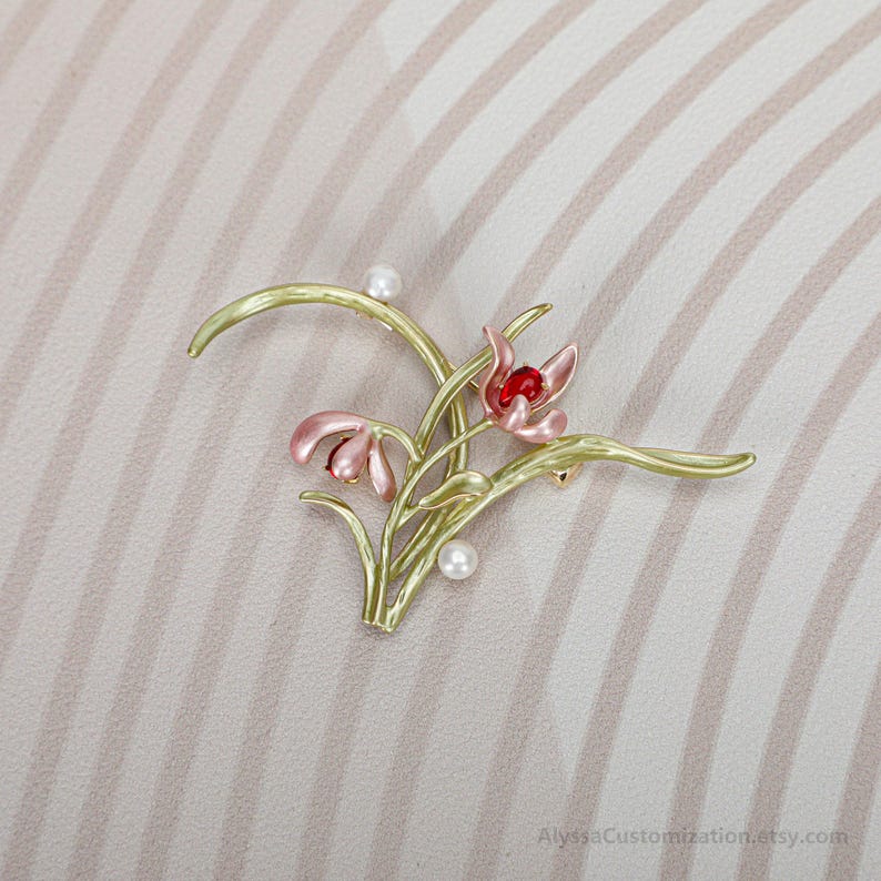 Puede incluir: Un broche floral con tallos y hojas de color verde claro, dos capullos de flores rosas con centros rojos y dos peque&ntilde;os acentos esf&eacute;ricos blancos. El dise&ntilde;o es delicado y bot&aacute;nico, con un acabado pulido. El texto AlyssaCustomization.etsy.com es visible.