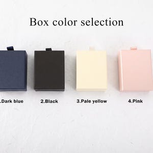 Puede incluir: Cuatro cajas de regalo rectangulares dispuestas en fila con el texto Box color selection encima. Las cajas est&aacute;n etiquetadas como 1.Dark blue, 2.Black, 3.Pale yellow y 4.Pink, cada una con una peque&ntilde;a leng&uuml;eta en el borde superior.
