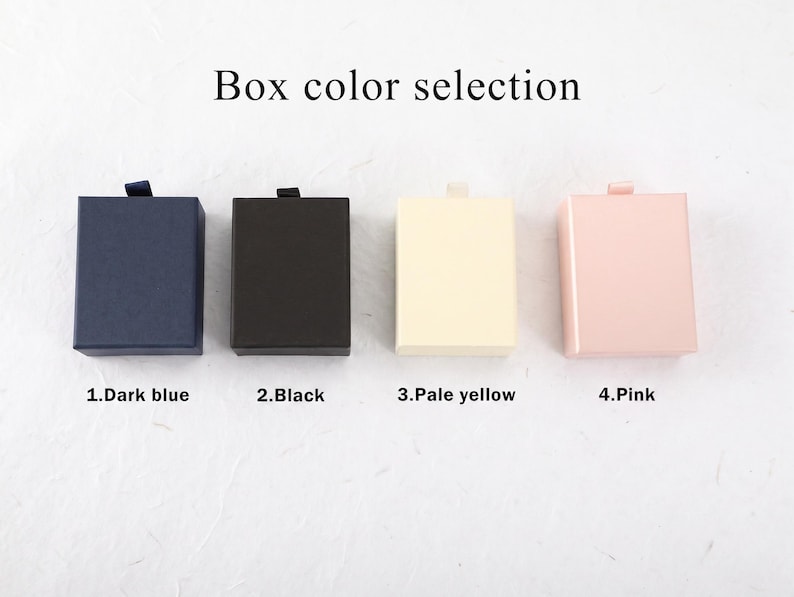 Puede incluir: Cuatro cajas de regalo rectangulares dispuestas en fila con el texto Box color selection encima. Las cajas est&aacute;n etiquetadas como 1.Dark blue, 2.Black, 3.Pale yellow y 4.Pink, cada una con una peque&ntilde;a leng&uuml;eta en el borde superior.
