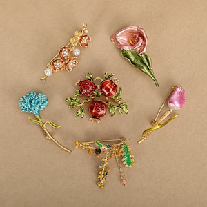 Puede incluir: Colección de seis broches florales. Los broches presentan varios diseños, incluyendo una flor azul, una cala rosa, un tulipán rosa, un racimo de granadas y una rama con flores naranjas y perlas. Los broches son de metal y esmalte.