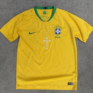 May include: A white ceramic mug with a black handle and the text "But First, Coffee" in a bold, black font. The mug is set against a blurred background, suggesting a cozy setting.