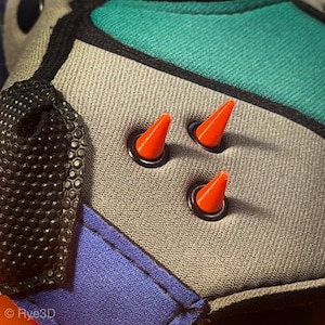 May include: A gray fabric accessory featuring three bright orange cone-shaped spikes set in black circular grommets. The item includes panels of teal and blue fabric, black textured trim, and the text "rye3d" printed in white on the lower left corner.