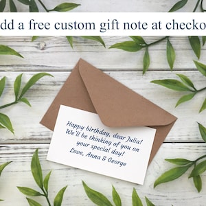 May include: A brown envelope and a white card with a handwritten birthday message. The card reads "Happy birthday, dear Julia! We'll be thinking of you on your special day! Love, Anna & George." Text at the top says "Add a free custom gift note at checkout."