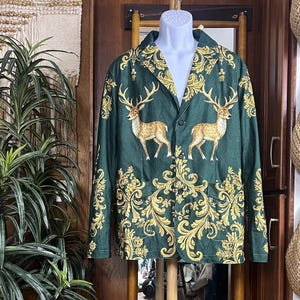 Pode incluir: Um blazer verde-escuro com um padrão repetitivo de volutas douradas e duas ilustrações de veados na parte frontal. A peça possui lapela entalhada, mangas compridas e três botões escuros no fecho central da parte da frente.