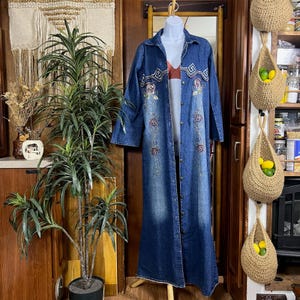 May include: A white ceramic mug with a black handle and the text "But First, Coffee" in a black, handwritten-style font. The mug is on a white surface.