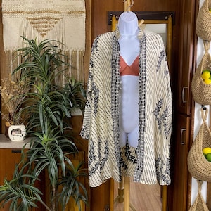 May include: A cream-colored kimono-style jacket with a black and white striped pattern and floral accents. The jacket is displayed on a mannequin. A burnt orange bra is visible underneath.