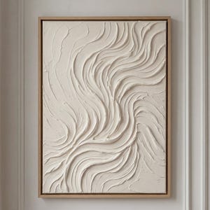 May include: Abstract textured wall art in a natural cream color, framed in a light wood. The artwork features a flowing, wave-like pattern created with thick brushstrokes, adding depth and dimension to the piece.