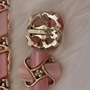 Puede incluir: Pendientes vintage rosas con clip, con dise&ntilde;o floral. Los pendientes presentan un centro rosa claro en forma de p&eacute;talo, rodeado por un marco de metal plateado. El mecanismo de clip se ve en la parte posterior. Sobre un fondo blanco y esponjoso.