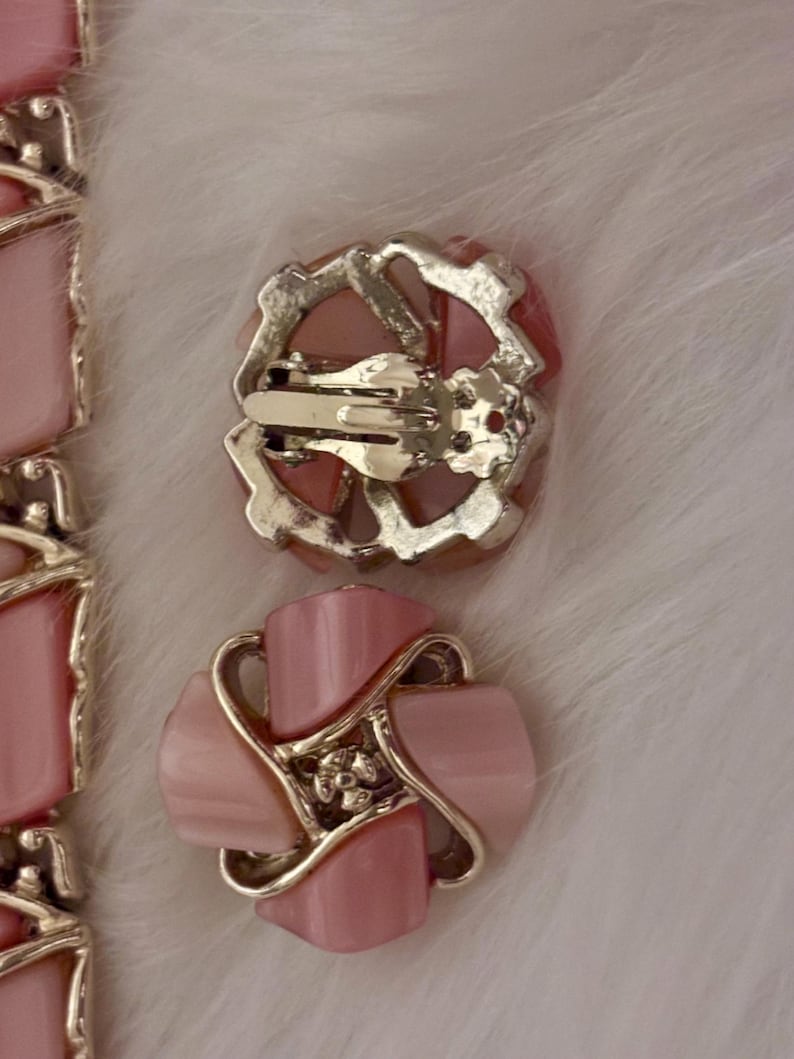 Puede incluir: Pendientes vintage rosas con clip, con dise&ntilde;o floral. Los pendientes presentan un centro rosa claro en forma de p&eacute;talo, rodeado por un marco de metal plateado. El mecanismo de clip se ve en la parte posterior. Sobre un fondo blanco y esponjoso.