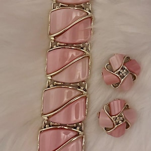 Puede incluir: Un conjunto de joyas vintage con pulsera y pendientes a juego. La pulsera tiene piedras rosas rectangulares engastadas en metal dorado. Los pendientes tienen forma de flor con p&eacute;talos rosas y un acento central.