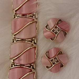 Puede incluir: Un conjunto de joyas vintage con pulsera y pendientes a juego. La pulsera y los pendientes tienen un dise&ntilde;o rosa claro en forma ovalada con detalles met&aacute;licos dorados. Los pendientes tienen forma de flor con un peque&ntilde;o centro brillante.