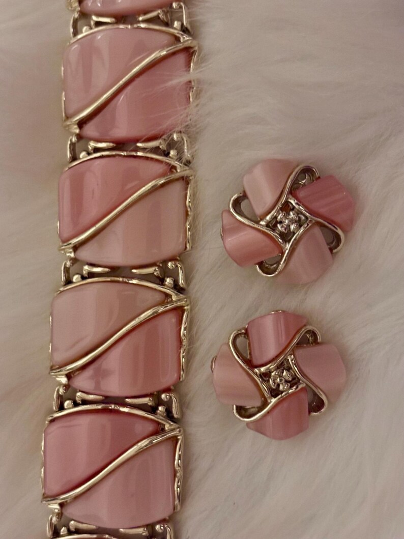 Puede incluir: Un conjunto de joyas vintage con pulsera y pendientes a juego. La pulsera y los pendientes tienen un dise&ntilde;o rosa claro en forma ovalada con detalles met&aacute;licos dorados. Los pendientes tienen forma de flor con un peque&ntilde;o centro brillante.