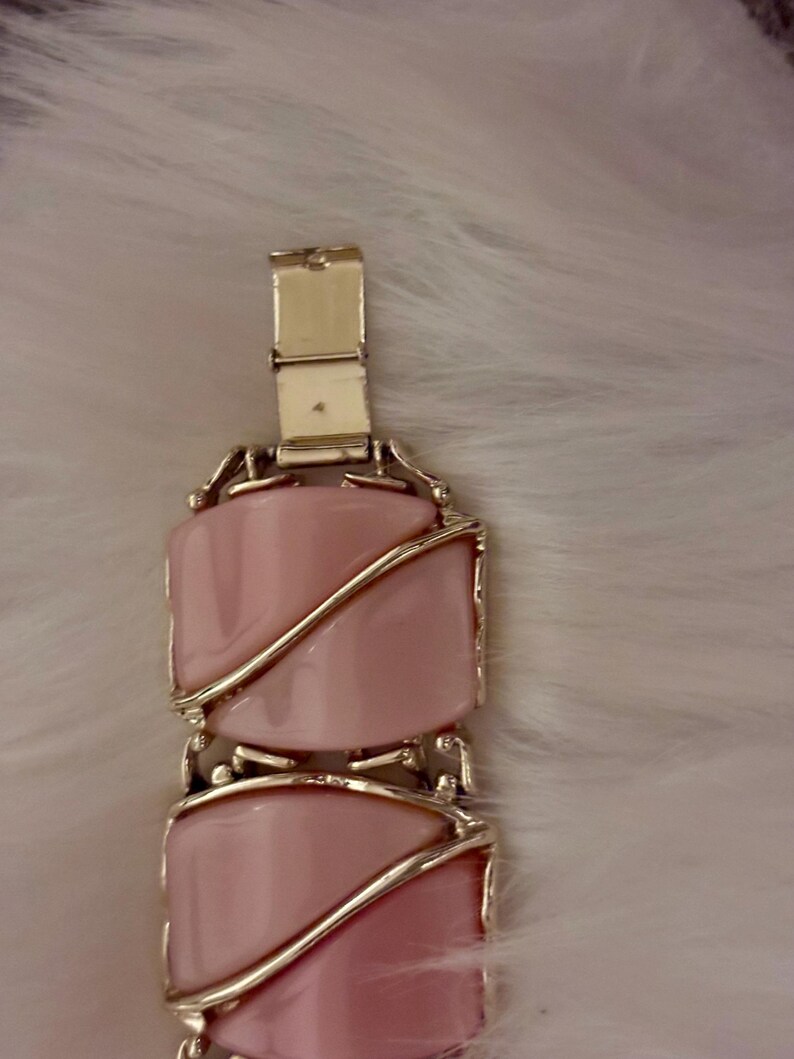 Puede incluir: Un brazalete vintage con piedras rosas rectangulares engastadas en metal dorado. El brazalete tiene un cierre de broche y un patr&oacute;n repetitivo de piedras rosas. El dise&ntilde;o es elegante y cl&aacute;sico, adecuado para diversas ocasiones.