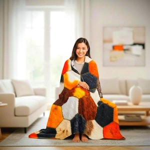 May include: A patchwork blanket featuring a geometric design in shades of orange, brown, black, and white. The blanket is draped over a person. The blanket's design creates a cozy and inviting scene. The blanket appears soft and warm.