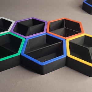 Könnte beinhalten: Ein Satz schwarzer, sechseckiger Aufbewahrungsbehälter mit farbigen Rändern. Die Behälter sind in einem Wabenmuster angeordnet, mit weißen, grünen, lila, orangefarbenen, blauen und gelben Rändern. Jeder Behälter ist in zwei Fächer unterteilt.