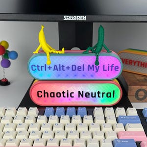 May include: A mechanical keyboard with pastel-coloured keycaps, including pink, blue, and white. Two illuminated bars with the text "Ctrl+Alt+Del My Life" and "Chaotic Neutral" sit atop the keyboard. A yellow banana and a green cucumber are perched on the bars.